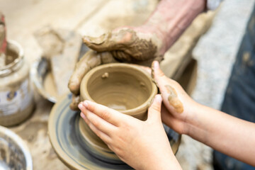 Fototapeta na wymiar Child learning pottery from an old potter. Passing traditions on trough generations. Handicraft