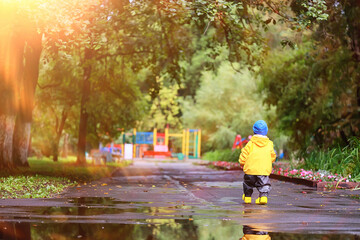 boy playing outdoors in puddles, autumn childhood rubber shoes raincoat yellow