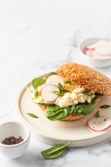 Breakfast burger with scrambled eggs, spinach, radish slices on white marble kitchen table, copy space for text