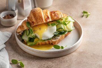 Delisious breakfast with croissant sandwich with fried egg, cheese, cucumber and micro greens and coffee over beige background. Healthy delicious breakfast with text space