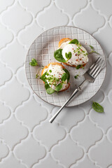 Poached egg sandwich with cream cheese, spinach and micro greens. Healty breakfast bruschetta on white tile background. Keto diet, text space, top view