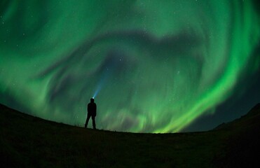 Obraz na płótnie Canvas Unidentified man enjoying the Northern Lights (Aurora Borealis) during a Solar Storm. Low light condition.