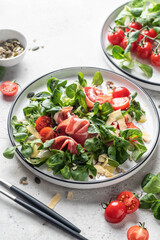 Green salad with ham or prosciutto, corn salad leaves, tomatoes and cheese. Healthy diet lunch on white marble background