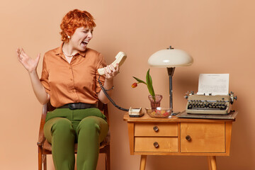 Businesswoman effortlessly manages own affairs from cozy home office screams loudly holds handset being very angry after telephone conversation sits on vintage chair surrounded by nostalgic furniture