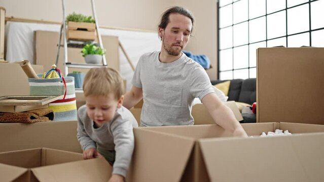 Father and son unpacking cardboard box at new home