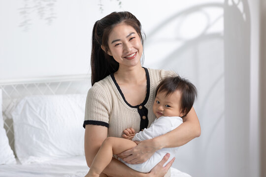 Asian mom holding her baby newborn in hand laughing sweet and lovely. Good moment of Happy mother and infant baby looking together smile with love. Wellness family. Mother and baby newborn Concept