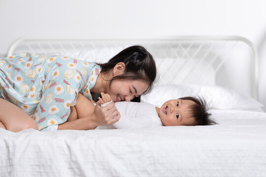 Asian mom playing with her baby boy smile and happiness together. Little baby toddler lying on bed and relax with mother speding time to learning and growth. Good momen of family time. Mother day