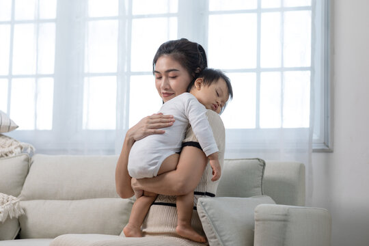 Happy Asian mother holding a cute newborn baby sleep on arm comfort and safety. Happy infant baby sleep with mother standing near windows warm and relax. Good moment. Mom and Baby care Concept