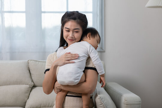 Happy Asian mother holding a cute newborn baby sleep on arm comfort and safety. Happy infant baby sleep with mother standing near windows warm and relax. Good moment. Mom and Baby care Concept