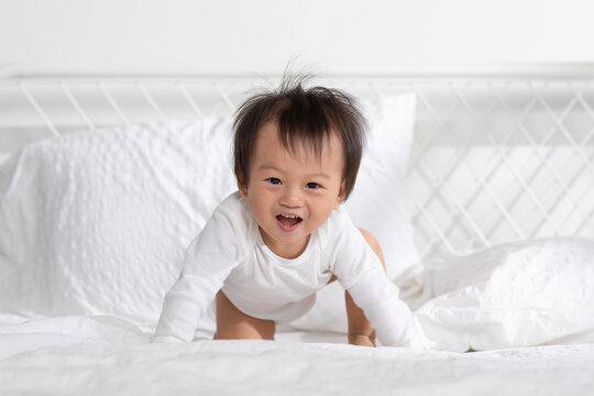 Asian baby toddler lying on white bed smile and looking at camera. Happiness little baby playing and practice of tummy time on bed at home. Baby Develop and Growth Concept