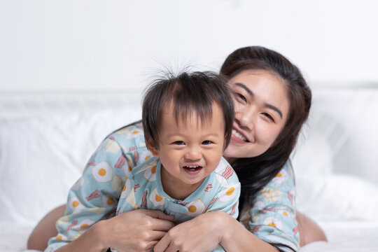 Cute Asian mom hugging her baby boy on bed smile and happiness together. Little baby toddler sit on bed and relax with mother speding time to learning and growth. Good momen of family time. Mother day