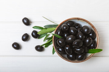Black olives in a bowl with leaves on a textured white wood background. Delicious and healthy food. Delicacy. Ingredient for salad and cocktails.Mediterranean Kitchen. Close-up. Place for text. 