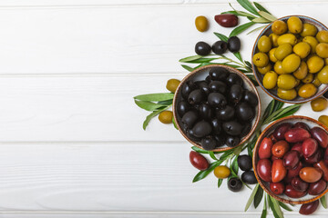 Set of green, red and black olives on a white background. Various types of olives in bowls and olive oil with fresh olive leaves. Delicacy.Mediterranean Kitchen. Copy space.