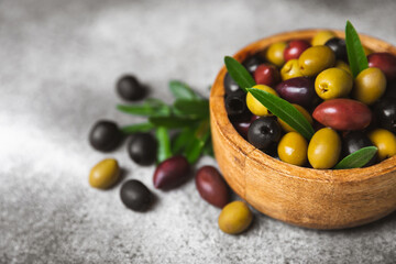 A set of green, red and black olives on a black marble background. Different types of olives in bowls and olive oil with fresh olive leaves. Delicacy.Mediterranean Kitchen. Copy space.