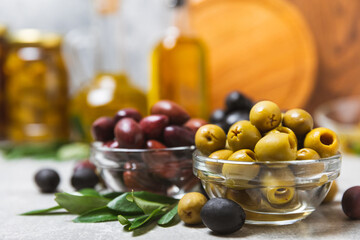 Set of green, red and black olives on a blue background. Different types of olives in bowls and olive oil with fresh olive leaves. Delicacy.Mediterranean Kitchen. Copy space.