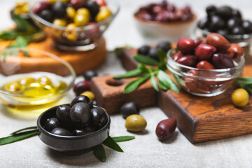 Set of green, red and black olives on a blue background. Different types of olives in bowls and olive oil with fresh olive leaves. Delicacy.Mediterranean Kitchen. Copy space.