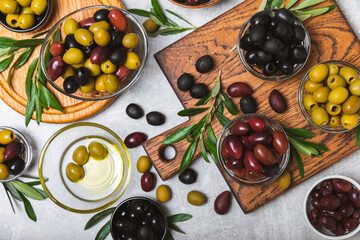 Set of green, red and black olives on a blue background. Different types of olives in bowls and olive oil with fresh olive leaves. Delicacy.Mediterranean Kitchen. Copy space.