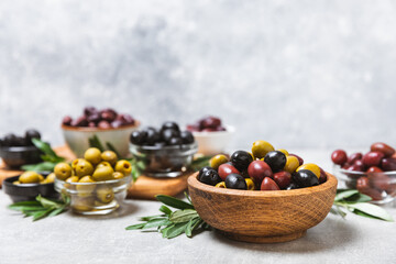 Set of green, red and black olives on a blue background. Different types of olives in bowls and olive oil with fresh olive leaves. Delicacy.Mediterranean Kitchen. Copy space.