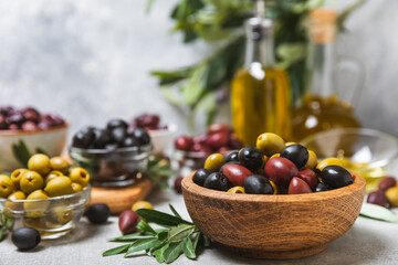 Set of green, red and black olives on a blue background. Different types of olives in bowls and olive oil with fresh olive leaves. Delicacy.Mediterranean Kitchen. Copy space.