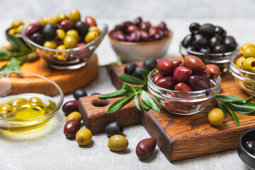 Set of green, red and black olives on a blue background. Different types of olives in bowls and olive oil with fresh olive leaves. Delicacy.Mediterranean Kitchen. Copy space.