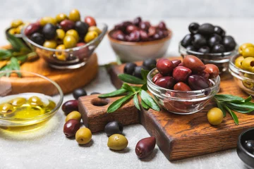 Foto op Plexiglas Set of green, red and black olives on a blue background. Different types of olives in bowls and olive oil with fresh olive leaves. Delicacy.Mediterranean Kitchen. Copy space. © Avocado_studio