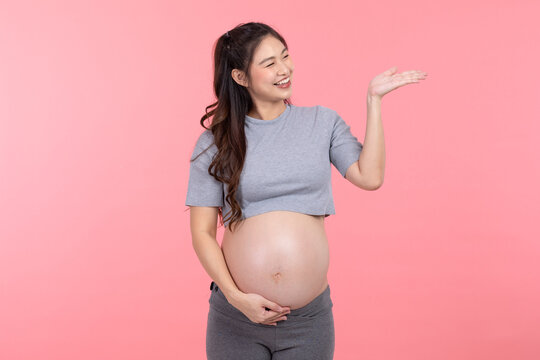 Happy Pregnant Woman standing smile stroking big belly with love and open palm isolated on pink background,Pregnancy of young woman enjoy with future life,Motherhood and Pregnant Concept