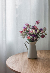 Fototapeta na wymiar Bouquet of summer wildflowers in an enameled jug on a round wooden table