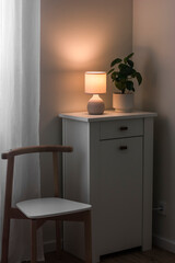 Cozy evening - ceramic lamp on the dresser, home flower, chair. Scandinavian style interior