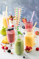 Fresh fruit smoothies with colourful straws surrounded by pieces of fruit.
