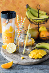 An empty glass jar mug with a straw waiting on a blended mango citrus smoothie.