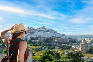 Young elegant  tourist with hat looking at Ostuni, the white city  in the south of italy - obrazy, fototapety, plakaty