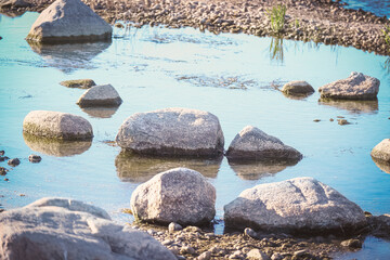 Close up of rocks on the river bank near blue water puddle on sunny day