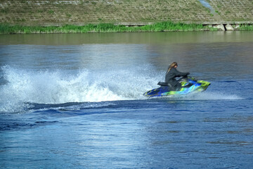 A young woman in a black jacket rides a water bike on a river in summer with motion blur