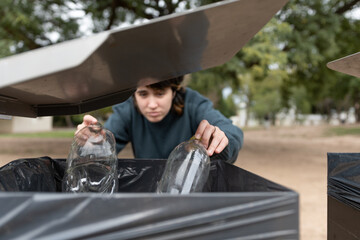 Naklejka premium Young woman depositing plastic bottles for recycling, hands in focus and body out of focus. Selective focus.