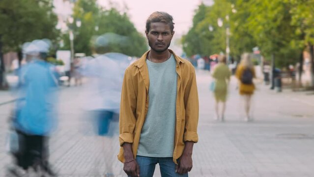Time lapse portrait of Indian guy standing in busy street with stream of people moving around. Busy life and young people concept.