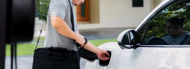 Progressive asian man install cable plug to his electric car with home charging station in the...