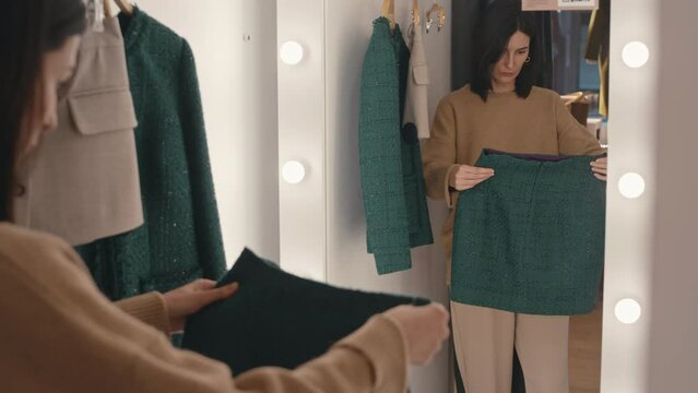 Medium shot of young good looking Caucasian woman trying on green tweed mini skirt in fitting room of luxury designer clothes store
