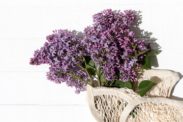 A branches of lilacs in mesh bag on white wooden background with a shadows. Natural background with empty space
