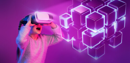 Naklejka premium Excited little girl wearing vr glasses enjoying online game with glowing neon virtual cubes, neon purple background