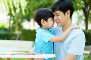 Happy lovely Asian father and son enjoy relaxing in picnic in the garden together, boy hugs his daddy. 