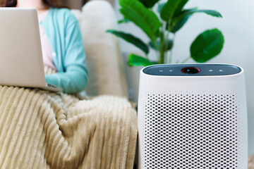 Asian woman relaxing in the cozy living room and using air purifier machine, using an air purifier machine to purify a pulluted air in residence.