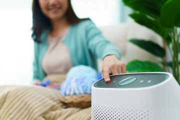 Happy Asian young woman turning on high efficiency air purifier while staying and relaxing in the...