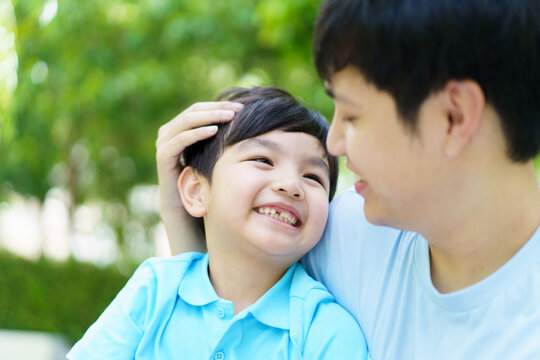 Happy lovely Asian father and son enjoy relaxing in picnic in the garden together, boy hugs his dad.
