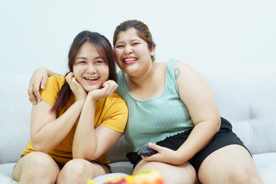 Happy cheerful Asian women sitting on a sofa in living room and watching a movie on tv together.