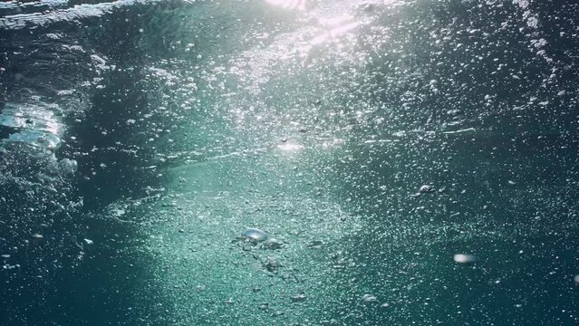 Motion of air bubbles rise up to surface in blue water at sunset in sunshine, Backlight (Contre-jour), slow motion. Sun beams penetrate water surface on bubbles rising underwater