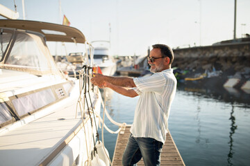 Senior Man Docking His Sailboat At Marina Using Rope Outside