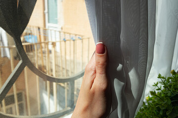 Woman's hand sliding curtain by window at home. 