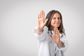 Reluctant and displeased senior woman doctor saying no, showing refusal gesture, telling to stop or...