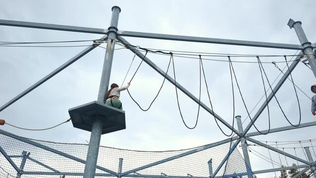Child girl with dad walks on a rope bridge, having fun in a rope adventure park, spending time outdoors. Scout practicing rappelling