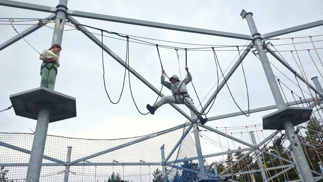 Child girl with dad walks on a rope bridge, having fun in a rope adventure park, spending time outdoors. Scout practicing rappelling